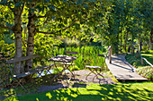 Seating area next to jetty on lake in sunny garden