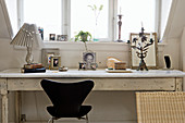 A designer chair at a old white desk with photos under a dormer window