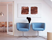 Two light blue armchairs under the abstract painting and a cat by the door