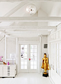A golden Buddha in front of French windows in a white room with wooden beams