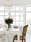 Barockstuhl am weißen Tisch mit Rosenstrauß unterm Kronleuchter