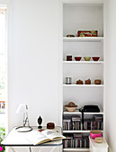 White shelf with small bowls and CD-s, in front of it a small table with reading lamp