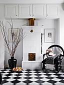 Black lacquered chair next to tiled stove, fruit bowl and floor vase on a black and white tiled floor