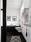 Toilet and bathtub in the bathroom with white walls and black painted wooden floor
