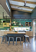 Metal stools around high table in open-plan kitchen in shades of grey and green
