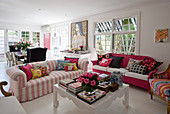 Sofas with scatter cushions around white coffee table holding books, boxes and vase of roses in open-plan living room
