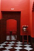 Old wooden door and surround in red wall in room with tiled chequered floor
