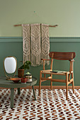 Makramee-Wandbehang, davor Stuhl und runder, niedriger Tisch auf gemustertem Teppichboden