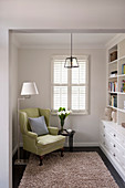 Lime-green wing-back chair, standard lamp and side table opposite fitted bookcases in living room