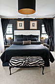 Double bed with black accessories and white headboard in bedroom with black wall and zebra-patterned bedroom bench