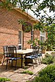 Solid wooden table and black metal chairs on veranda outside brick house