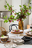 Branches of redcurrants in vase and cake on set table