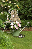 Bouquet of peonies in watering can next to chair in front of box hedge and climbing rose
