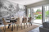 Set dining table with upholstered chairs in front of monochrome mural wallpaper