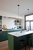 Barstools at island counter in kitchen with dark green cupboards
