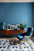 Retro armchair, sideboard and rug in living room with blue wall