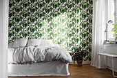 White bed with valance against leaf-patterned wallpaper in bedroom