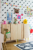Wooden sideboard in child's bedroom with horse-patterned wallpaper and colourful accessories