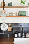 Shelves above black tiled splashback in vintage-style kitchen