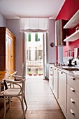View through long, narrow kitchen with white counter against red wall in small apartment