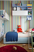 Bett und Hängeregal vor bunt gestreifter Wandtapete in Kinderzimmer