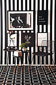 Chair and side table in black-and-white seating area with pictures on striped wallpaper