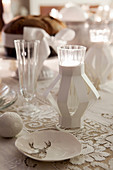 White, festive arrangement with lace tablecloth and tealight holders on table