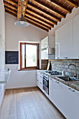 Küche in toskanischem Landhaus mit weißen Küchenfronten und Holzdeckenkonstruktion