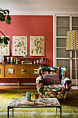 Patterned armchair in front of botanical illustrations on coral-red wall