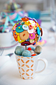 Ball decorated with brightly coloured buttons in mug of pompoms