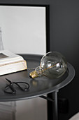 Scissors, light bulb and book on round, charcoal-grey side table