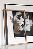 Pressed plant sprig between plates of glass in frame in front of portrait of woman