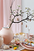 Wooden eggs hung from flowering branch in vase on Easter table set in pink