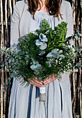 Frau hält einen grünen Strauß mit Zweigen und Blumen im Boho-Stil