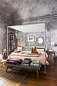 Modern metal four-poster bed with blankets and bed linen on bedroom bench at foot