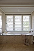 Weiße Badewanne mit beigefarbener Marmoreinfassung in Nische am Fenster