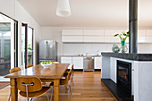 Dining table, chairs and fireplace in front of white kitchen counter in open-plan interior