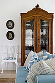 Scatter cushions on pale blue sofa, antique display case and chair in living room