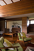 Wohnzimmer mit grünen Sesseln im Fiftiesstil, Dielenboden und diversen Holzverkleidungen