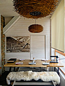 Sheepskin rug on bench at set dining table below pendant lamp made from branches