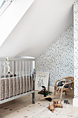 Cot below sloping ceiling in attic nursery with star-patterned wallpaper