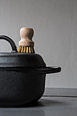 Black cooking pot with lid and wooden brush