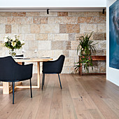 Black upholstered chairs around wooden table in dining room with stone wall