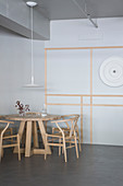 Designerstühle um runden Holztisch vor grauer Wand mit Zierleisten