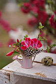 Posy of geraniums, fuchsia, feather and apple twig in tiny watering can