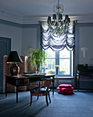Antique desk, chandelier and gathered blinds in stylish blue-grey study