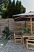 Shallow wicker basket planted with herbs in seating area with parasol on gravel terrace