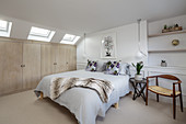 White bedroom with beige fitted wardrobes below sloping ceiling with skylights