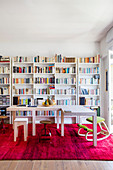 Two three-legged tables arranged in an L on hot-pink rug in front of bookcase