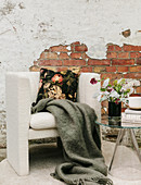 Woollen blanket and floral cushions on armchair against brick wall